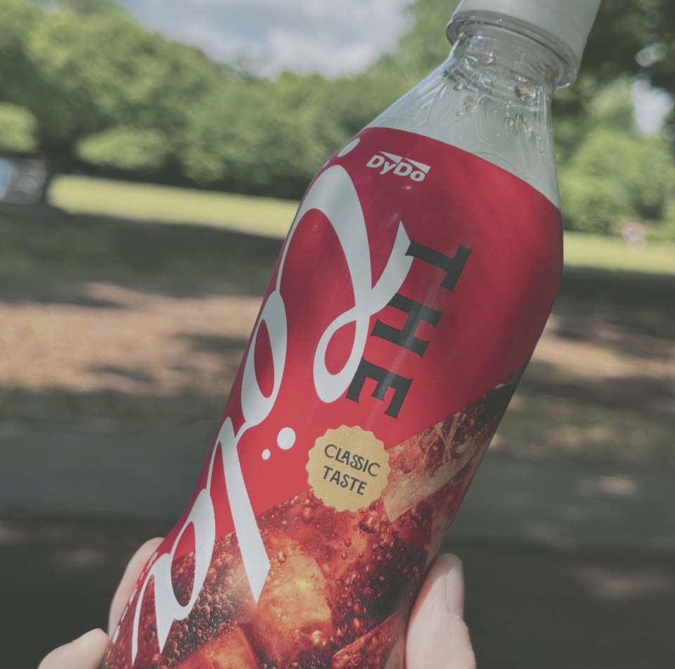 公園の緑を背景に「コーラクラシックテイスト」と書かれたコーラのペットボトルが写っている