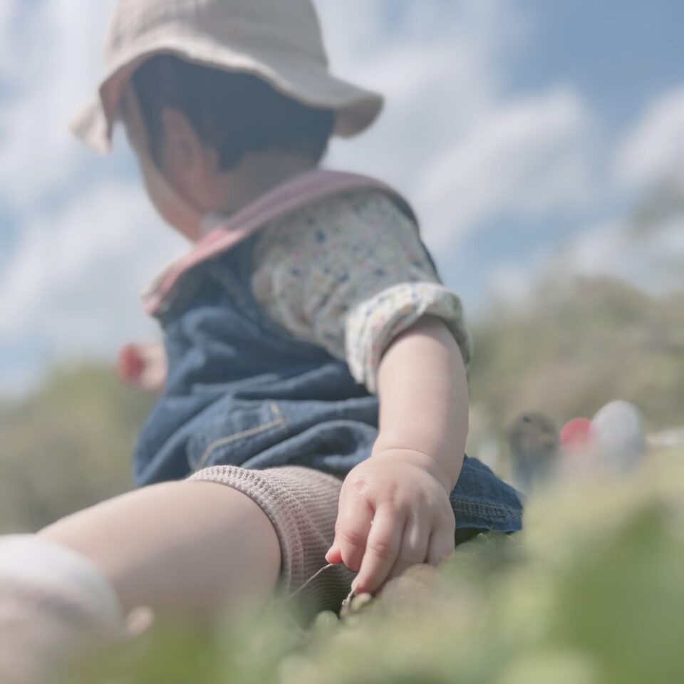 芝生の上にピンク色の帽子を被った女の子が座っている