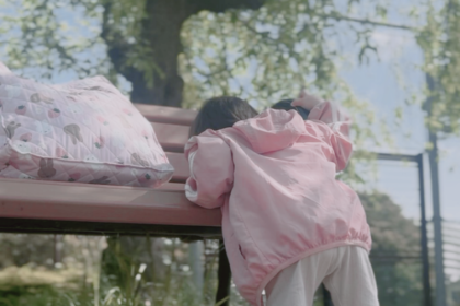 公園のベンチにピンクのバッグが置いてありピンク色の服を着た女の子がつかまり立ちをしている